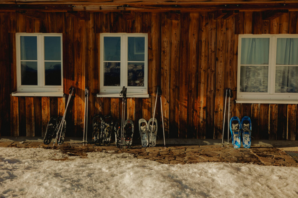Skistöcke und Schneeschuhe lehnen von außen an einem gemütlichen verschneitem Holzhaus